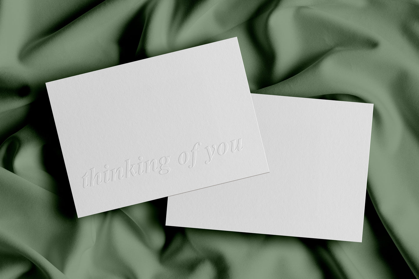 A plain white greeting card with 'thinking of you' embossed on the front